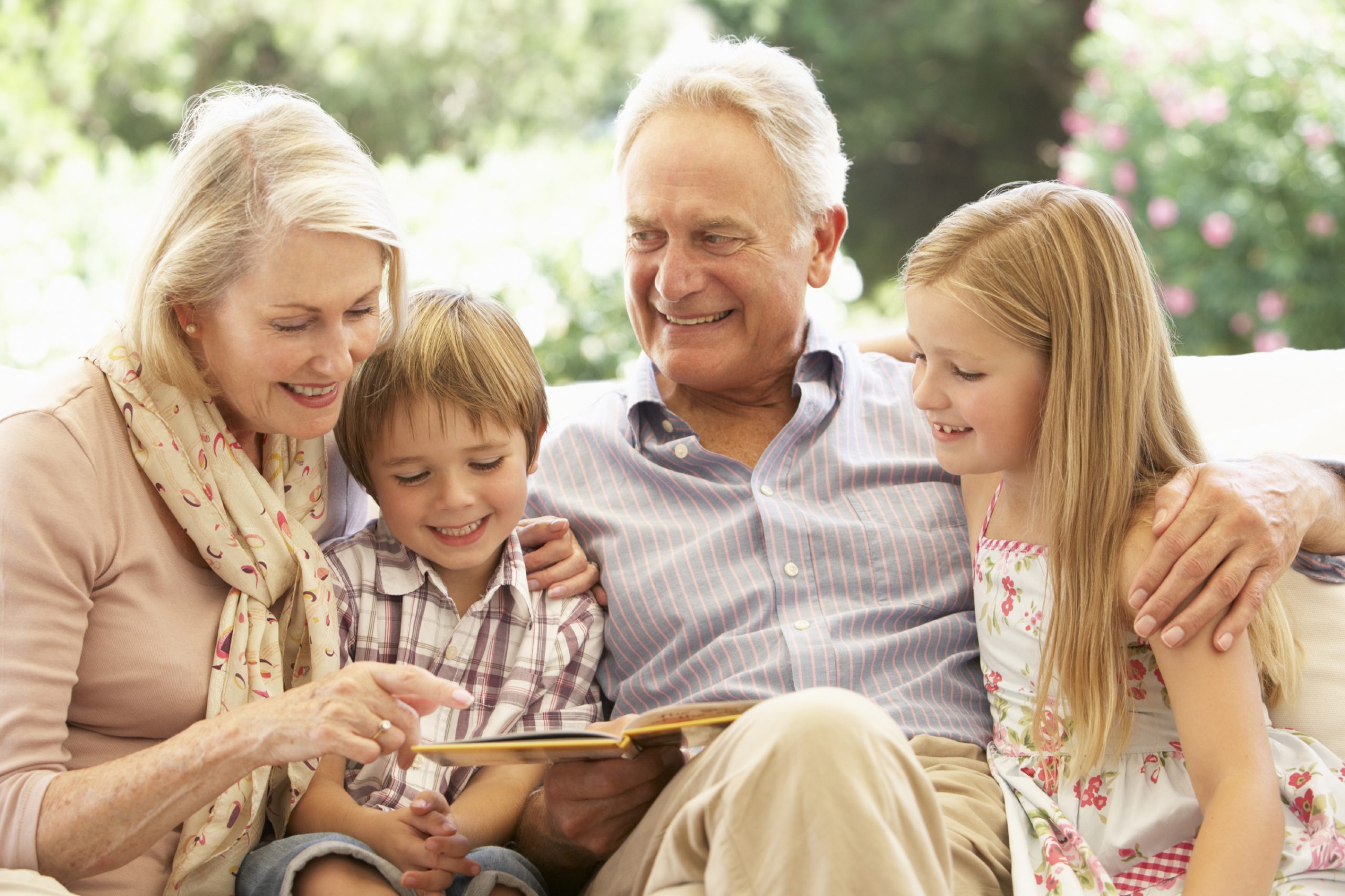 Portrait Of Grandparents Reading To Grandchildren On Sofa